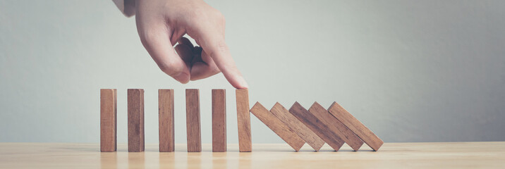 Hand stopping wooden domino business crisis effect or risk protection concept