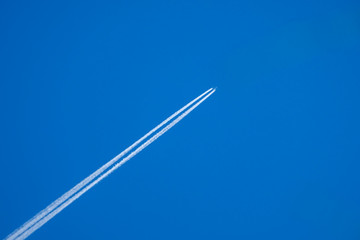 White jet passenger plane flying at high altitude in a blue clear cloudless sky. Behind the aircraft is a white condensation trail of water vapor. - obrazy, fototapety, plakaty