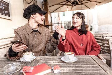 Loving couple quarrel at the bar. On the table are placed a red book and two gifts with red bow. Couple is drinking cappuccino.