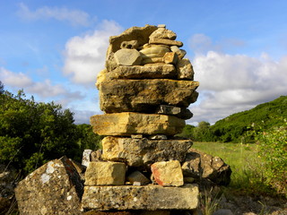 Balanced stones on a background of blue sky and green trees. Stone tower, balanced rock sculpture.