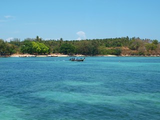 Motor vessel with people floating on the sea. Shore on the horizon. Forest, sand, beach. View from the water to the shore. Longtail boat. Thailand, Andaman Sea, Phuket. Seascape, landscape, panorama. 