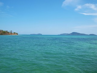 Fototapeta na wymiar Sea and islands on the horizon. Cliff with palm trees in a distance. Blue sky and transparent white cloud. Azure water with ripples. Thailand resort. Tropical paradise. Seascape. Andaman sea, Phuket. 