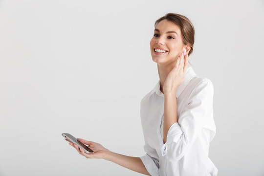 Image of smiling woman using wireless earphone and mobile phone