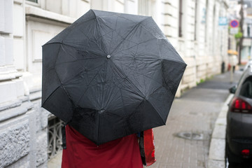 Portrait of woman walking in the street wearing a red coat and a black umbrella