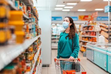 Shopping trip. A young, pretty Caucasian woman with a medical mask on her face selects products in a store. Product purchase concept and the coronovirus pandemic