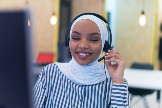 African Muslim Female With Hijab Scarf Customer Representative Business Woman With Phone Headset Helping And Supporting Online With Customer In Modern Bright Call Centre.