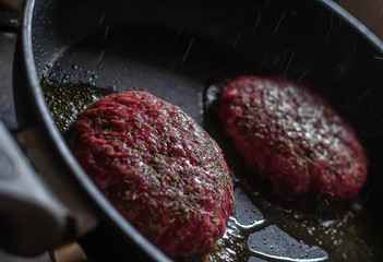 Two raw meat hamburgers cooking in oily frying pan