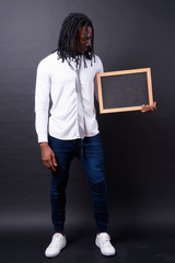 Full body shot of young handsome African businessman with dreadlocks holding blackboard