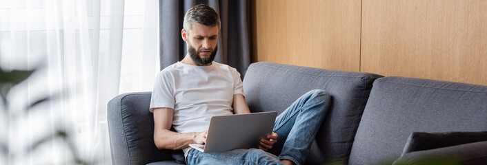 Panoramic orientation of handsome teleworker using laptop in living room