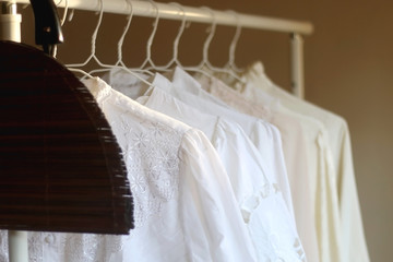 Vintage wooden bag and white blouses on a clothing rack. Selective focus.