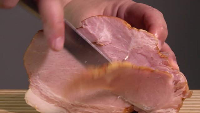 Unrecognizable male hand with knife cutting slicing ham on cutting board. Delicious taste, snacks, cooking process. Healthy food concept. European cuisine, kitchen interior. Close up view
