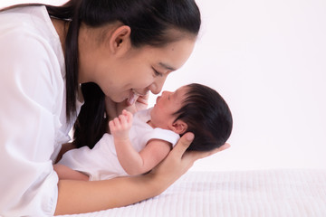 Close up beautiful young Asian mother kissing and hold tiny adorable newborn baby girl 0-1 month on white bed with caring and love, lifestyle health care newborn at home concept on white background
