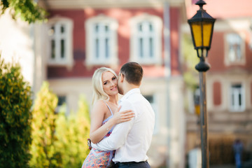 Fototapeta premium Lovely couple walking around the block. Dark-haired man in a white shirt hugging a blonde in a beautiful dress