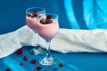 Dessert Panna cotta with currant berries in glasses on  leg is decorated with tea rose on blue background.