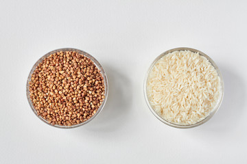 Raw white rice and buckwheat groats in a transparent glass plate on white background. Problem of choice. Closeup, top view