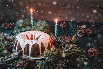 A large festive cupcake decorated with white icing and pastry topping, two blue burning candles,...