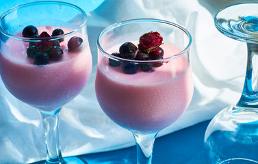 Dessert Panna cotta with currant berries in glasses on  leg is decorated with tea rose on blue...