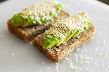 Sandwiches made from avocado and dark sesame bread. On a white plate is a sandwich with avocado and sesame seeds.