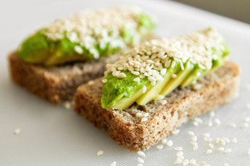 Sandwiches made from avocado and dark sesame bread. On a white plate is a sandwich with avocado and sesame seeds.
