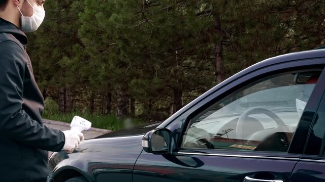 Security guy measures a driver's body temperature, fever with an infrared thermometer checking for coronavirus on the road