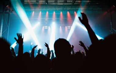 Audience with hands raised at a music festival and lights streaming from the stage.