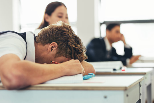 Bored high school student sleeping on classroom desk