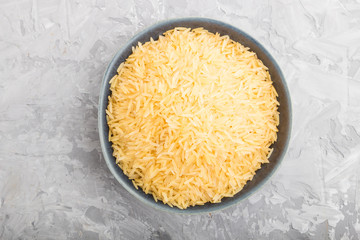 Blue ceramic bowl with raw golden rice on a gray concrete background. Top view.