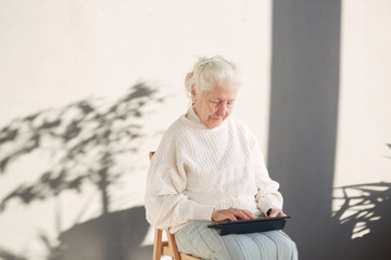 Grandmother is sitting in the chair and holding a tablet un her hand. Old women using tablet....