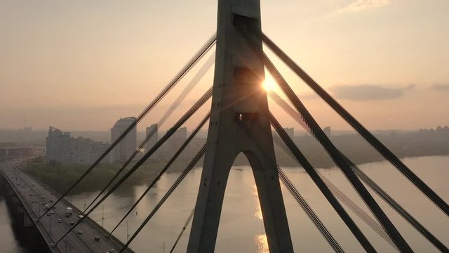 Aerial drone view View Of North or Moscow Bridge Kiev, Ukraine over Dnieper. Drone span between the cables of the bridge. Sunset sun. City view. Rays of the sun through the cables of the bridge
