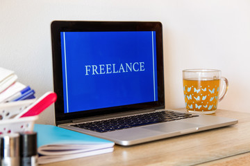 The laptop is on the table. Near the phone, cup, and cosmetics. On screen Freelance