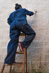 woman on top of a ladder painting by brushing the wall.