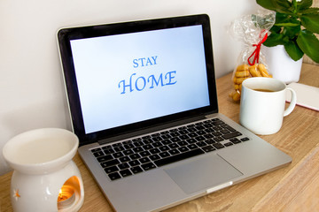 The laptop is on the table. Near the phone, cup, and cosmetics. On the screen the inscription Stay Home