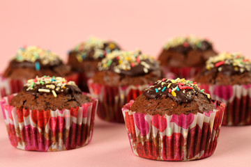 Homemade, delicious dark chocolate muffins with cocoa and colorful sugar sprinkles on a pink background. Selective focus and shallow depth of field