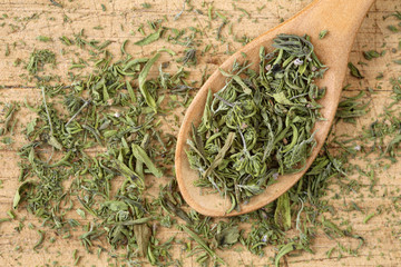 Top down view of dried summer savory in a wooden spoon, on a rustic wooden table. Close up of chopped, dry Satureja hortensis, a culinary and medicinial herb, with selective focus