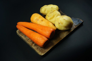 Raw peeled carrots and potatoes isolated on dark/black background