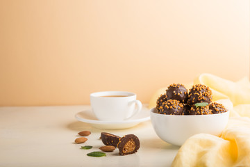 Chocolate caramel ball candies with almonds and a cup of coffee on a white and orange background. Side view, copy space.