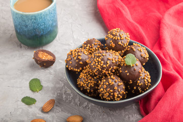 Chocolate caramel ball candies with almonds and a cup of coffee on a gray concrete background and red textile. Side view.