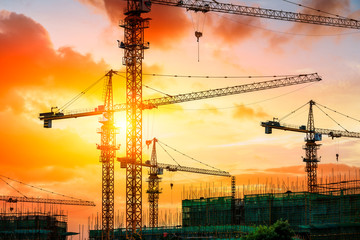 Tower crane and building construction site silhouette at sunrise.