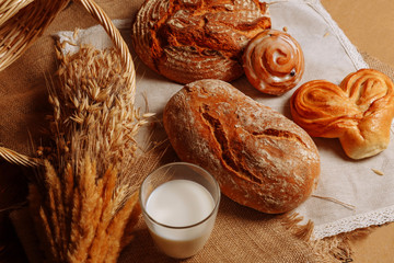 Fresh bread and pastries lie on the table close-up, next to a glass of milk and a sprig of wheat.