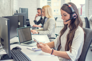 Female customer support operator with headset using phone in the office.
