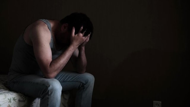 Sad pensive depressed man sitting on a bed in a dark room
