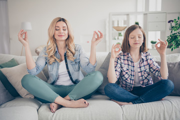 Photo of domestic charming blond lady mommy daughter relaxing comfy couch hold arms om yoga gesture stay home quarantine time spend weekend together eyes closed living room indoors - obrazy, fototapety, plakaty