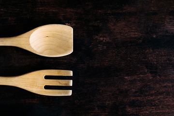 A wooden fork and spoon lie on a brown wooden table.