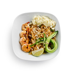 Fried udon noodles in a wok with shrimp and nuts. Served with fresh cucumber and lime. Traditional asian food.