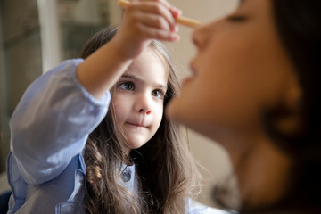 Fototapeta premium Happy loving family. Mother and daughter are doing make up and having fun at home. Close up portrait of daughter making up on her mom's face.