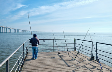 Fisherman with a fishing rod  near Vasco de Gamma Bridge. Lisbon, Portugal.