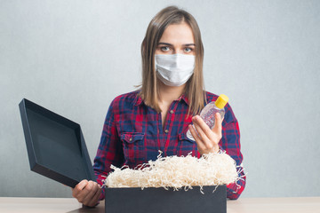 Woman wearing mask, opening cardboard black box and holding sanitizer gel