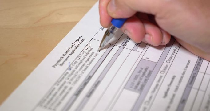 A closeup view of a business owner filling out the Paycheck Protection Program form. The PPP was a necessity for business owners during the 2020 COVID-19 pandemic to aid employee retention.	