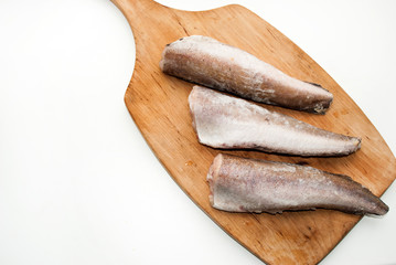 Three frozen hake fish. Headless fish on a wooden board.