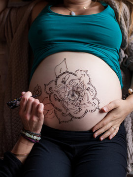 woman drawing Mehndi design on pregnant belly. Selective focus on belly.